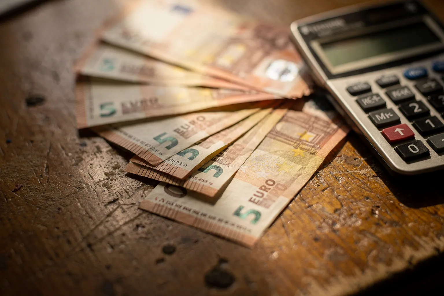 Euro-Banknoten liegen gefächert neben einem Taschenrechner auf einem Tisch